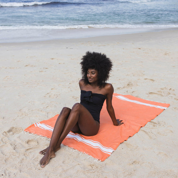 Femme allongée sur une fouta de plage couleur orange - BY FOUTAS