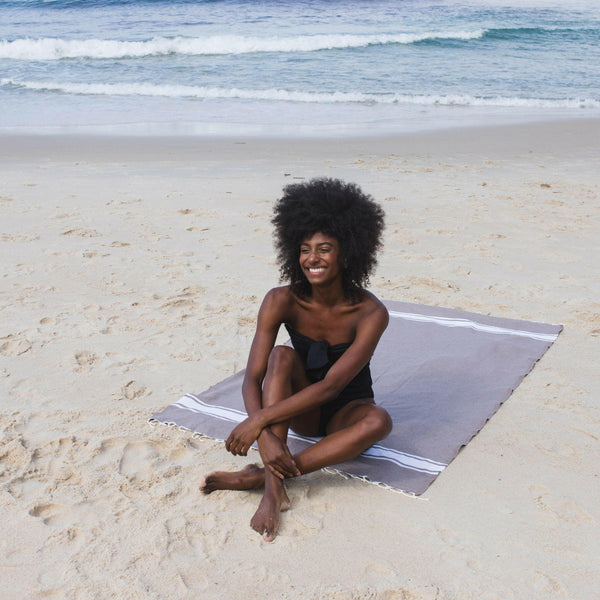 Woman lying on a taupe-colored beach fouta - BY FOUTAS