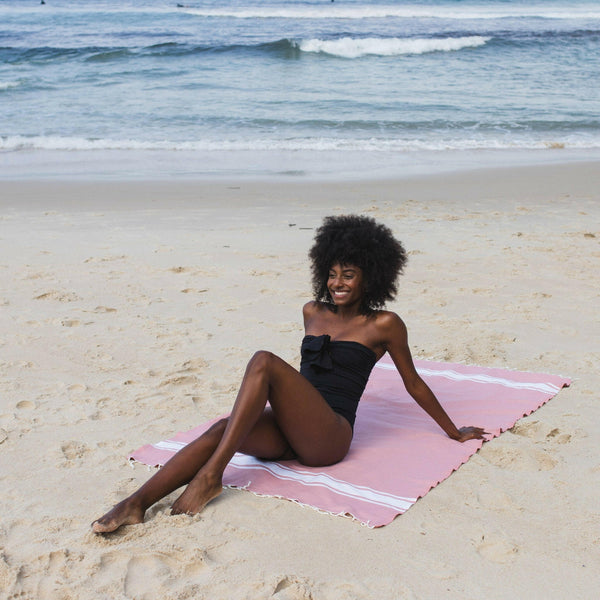 Woman lying on a baby pink beach fouta - BY FOUTAS