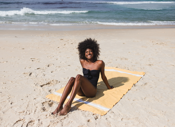 Woman lying on a mustard-yellow fouta on the beach | BY FOUTAS