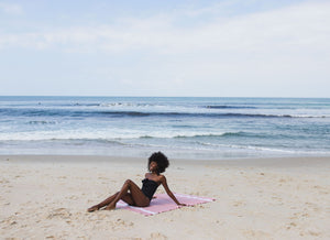 Mujer tumbada en la playa sobre una fouta rosa tejido plano - BY FOUTAS