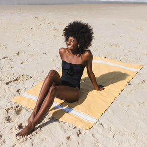 Donna sdraiata su una fouta da spiaggia giallo senape. BY FOUTAS